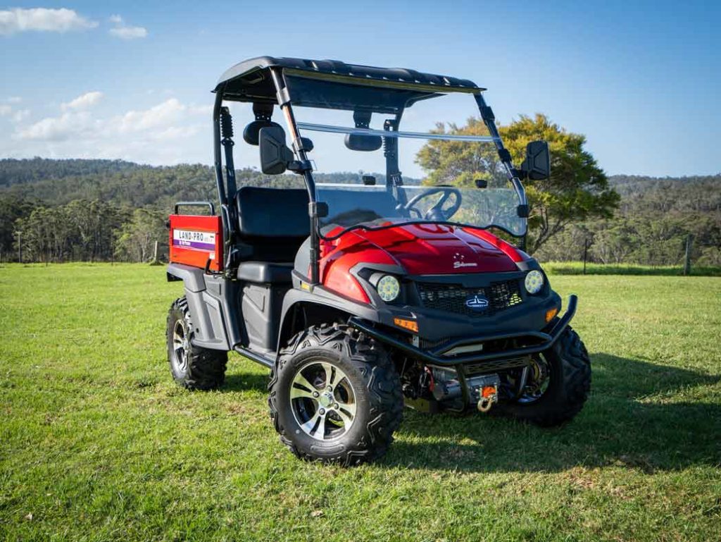 Ein rotes UTV steht auf einer sonnigen grünen Weide vor einer malerischen Hügellandschaft im Hintergrund.