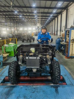 Ein Techniker in blauer Arbeitskleidung testet das Fahrwerk eines UTV-Rahmens in einer großen Montagehalle.