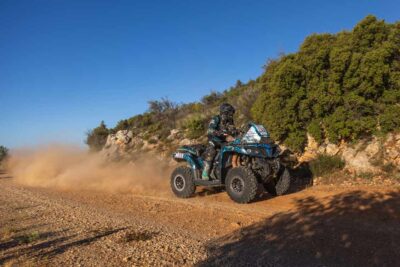 Ein Quad-Rennfahrer auf einem blauen ATV von CFMOTO, der eine Staubwolke auf einer unbefestigten Rennstrecke aufwirbelt.