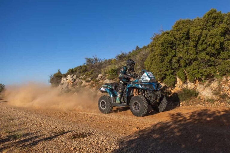 Ein Quad-Rennfahrer auf einem blauen ATV von CFMOTO, der eine Staubwolke auf einer unbefestigten Rennstrecke aufwirbelt.
